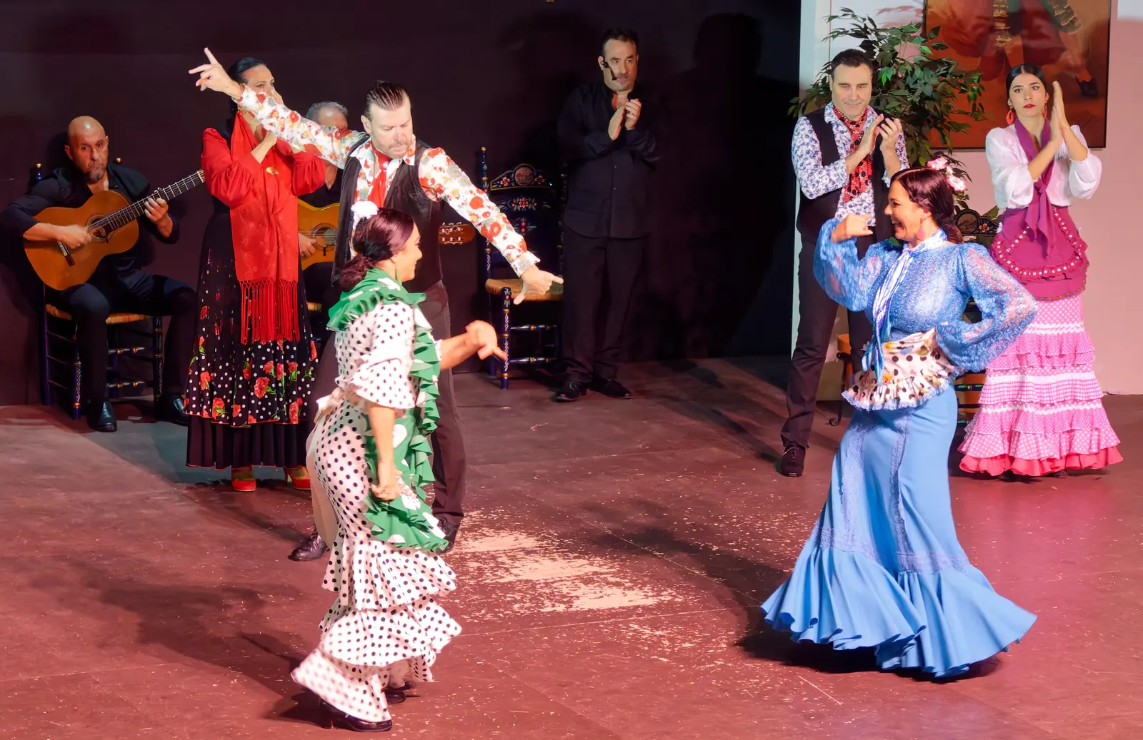 Ballerine in abiti blu, rosa, verdi e rossi si muovono sul palco mentre i chitarristi suonano dietro di loro